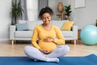 Genç zenci hamile kadın, koca göbekli müstakbel anne minder üzerinde yoga yapıyor oturma odasında bebek hareketlerinin keyfini çıkarıyor. Spor ve spor, evde tek başına sağlık hizmetleri ve bebek bekliyor.