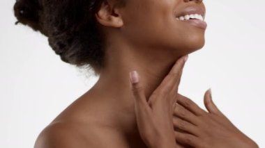 Kırışıklık önleyici vücut bakımı. Tanımlanamayan Afrikalı Amerikalı bir kadının boyuna krem sürerken, gülümserken, beyaz stüdyo arka planı, yavaş çekim.