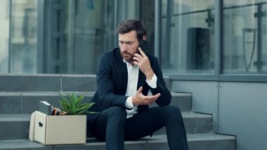 İşten çıkarma konsepti. İşsiz, orta yaşlı, arkadaşlarıyla telefonda konuşan, ofis binasının yanında oturan, ağır çekimde çalışan, serbest alan...