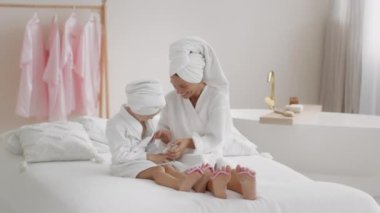 Mutlu aile eğlenceleri. Kaygısız anne ve kızı birbirlerini gıdıklıyor ve gülüyorlar, birlikte güzel bir gün geçiriyorlar, kafalarında havlularla ve bornozlarla oturuyorlar, ağır çekimde, boş alanda.
