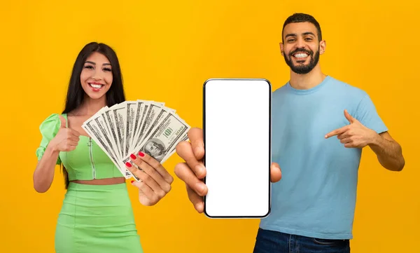 stock image Beautiful young middle eastern lovers won prize, giveaway concept. Happy arab man and woman posing with smartphone and money, pointing at cell phone blank screen, yellow studio background, collage