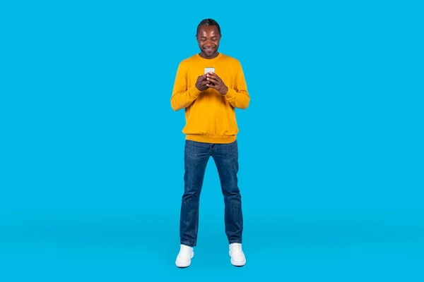 스튜디오 길이의 아프리카 미국인 남성의 평상복 촬영새로운 핸드폰을 파란색 배경에 — 스톡 사진