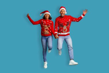 Noel Baba şapkası ve xmas kazak giyen, el ele tutuşan, Noel 'i birlikte kutlayan, mavi stüdyo arka planında izole edilmiş, genç ve duygusal bir çift.