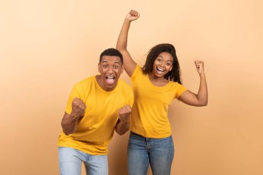 Vay canına, evet. Aşırı mutlu Afro-Amerikalı çift yumruklarını sıkmış ve kameraya bağırıyor, zaferi kutluyorlar şeftali rengi stüdyo duvarında izole edilmiş poz veriyorlar, afiş.