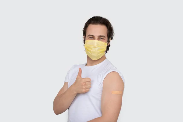 Usmívající Tisíciletý Běloch Ochranné Masce Ukazuje Rameno Náplastí Imunizaci Palec — Stock fotografie