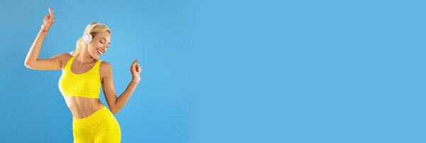 Wide Extended Banner With Young Sporty Woman Listening Music In Wireless Headphones And Dancing, Fit Lady In Sportswear Having Fun While Standing Isolated Over Blue Studio Background, Panorama