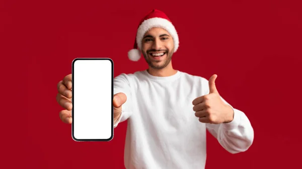 伟大的报价 快乐的阿拉伯男子在圣诞老人的帽子演示空白智能手机与白色屏幕和显示拇指向上 快乐的中东家伙推荐新的移动应用程序或网站 — 图库照片