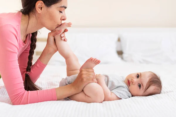 Vårda Unga Mamma Kysser Babys Fötter Medan Gör Gymnastik Sängen — Stockfoto