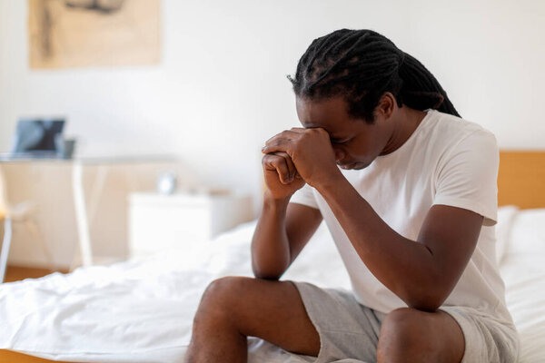 Seasonal Depression. Portrait Of Sad Young African American Man Sitting On Bed With Head Down, Upset Depressed Black Man Resting In Bedroom, Suffering Life Problems Or Mental Breakdown, Copy Space