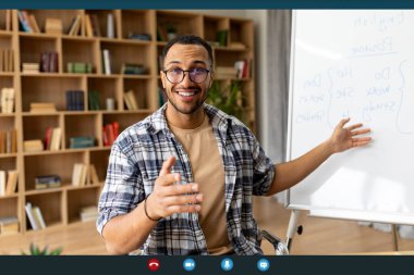 Uzaktan eğitim ve teknoloji. Genç Arap erkek öğretmen video konferansı yapıyor, yabancı dil dersi alıyor, web araması sırasında kamerayla konuşuyor, beyaz tahtanın yanında oturuyor.