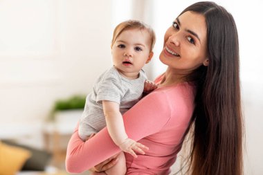 Anneliğin mutluluğu. Mutlu bir annenin portresi, ellerinde küçük şirin bir bebekle kameraya bakıyor, yatak odasında duruyor, evin içinde, boşluğu kopyalıyor.