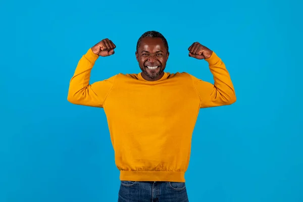 青いスタジオの背景で成功を祝う黄色の感情的なハンサムなアフリカ系アメリカ人の成熟した男 拳をきれいにし 叫んで スペースをコピーします 人間の感情やジェスチャーの概念 — ストック写真