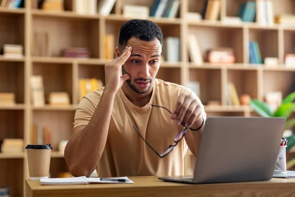悲伤疲惫的Arab男性自由职业者工作在笔记本电脑上 触摸着头 举着眼镜 看着电脑屏幕 坐在家里的工作场所 截止日期 工作过度 工作中的问题和压力 — 图库照片