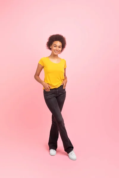 stock image Happy pretty millennial african american curly lady student in casual looking at camera, isolated on pink background, studio, full length, vertical. Study and work, offer and ad, sale, free space