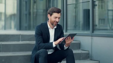 Tasasız orta yaşlı yönetici web sörfü dijital tablet üzerinde, açık havada eğlenme, ofis binasının yanındaki merdivenlerde oturma, yavaş çekim, serbest alan
