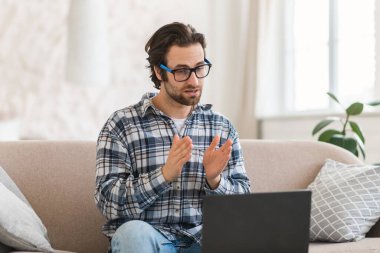 Gözlüklü, ciddi meşgul, Avrupalı genç bir adam video görüşmesi yapıyor. Oturma odasının iç tarafındaki kanepede bilgisayar başında toplanıyor. İş, iş, aygıtla serbest çalışma ve online sohbet, özel ders ve ders