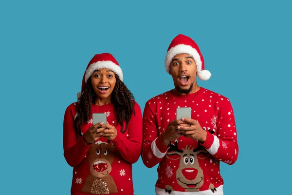 Amazed Young African American Couple Christmas Outfit Using Smartphones Blue — Stock Photo, Image