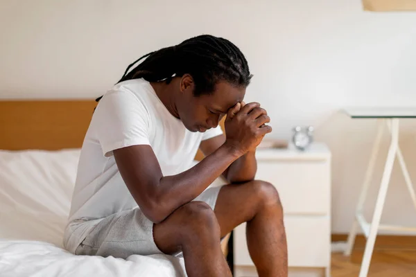 生活问题概念 沮丧的黑人男人低着头坐在床上 年轻的非洲裔美国男人感到孤独和不安 忍受季节性抑郁症或精神崩溃 复制空间 — 图库照片