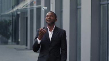 Başarılı bir iş. Orta yaşlı mutlu Afro-Amerikan iş adamının açık hava portresi. Büyük kârın tadını çıkarıyor, bir sürü parayla oynuyor ve gülümsüyor, yavaş çekim, serbest alan.