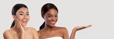 Banyo havlularına sarılı çok ırklı genç bayanlar gri arka planda kameraya gülümsüyor, duştan sonra vücut bakımının keyfini çıkarıyor, reklam, kolaj, afiş için fotokopi alanı gösteriyor.