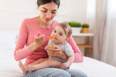 Sevimli küçük bir kız bebek kaşıktan yiyor, şefkatli bir anne tatlı bir bebeği püre ya da yulaf lapasıyla besliyor, çocuğa sağlıklı yiyecekler veriyor.