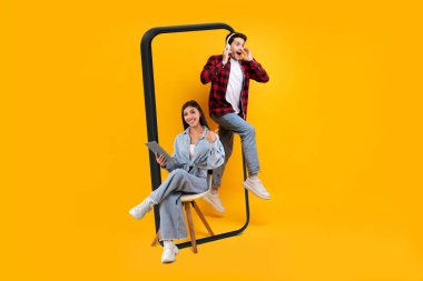 Kablosuz kulaklıklı genç beyaz adamın büyük akıllı telefondan atlamasına sevindim. Tabletli Asyalı kadın, turuncu arka planda izole edilmiş bir şekilde baş parmağını gösteriyor. Tavsiye, tavsiye, ses uygulaması ve eğlence