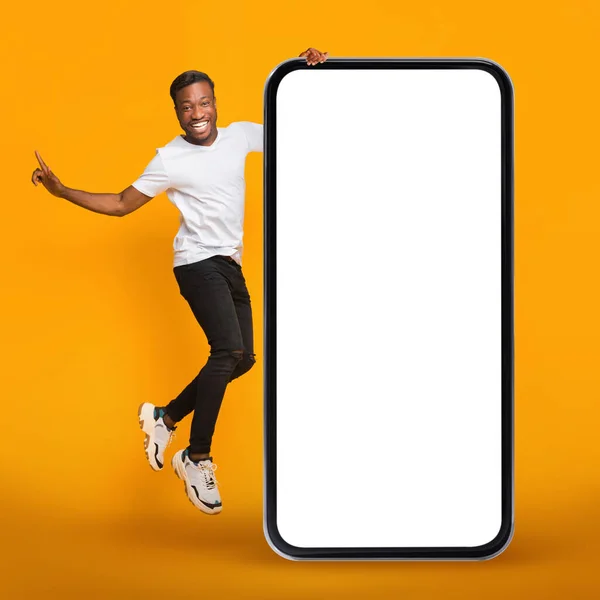 网上广告 快乐的黑人男子跳到巨大的空白手机旁边 带着白屏 快乐而兴奋的非洲裔美国人广告手机 或者推荐新网站 — 图库照片