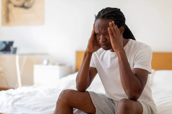 忧心忡忡的非洲裔美国年轻人坐在床上的画像 思考生活问题 头痛或急性偏头痛的黑人千年人的画像 — 图库照片