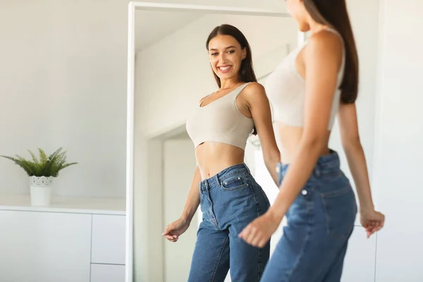 成功した減量と笑顔の後にポーズをとって 鏡の中で彼女の反射を楽しんで幸せな白人女性は 自宅でミラーの近くに立っている 痩身ダイエットの概念 — ストック写真