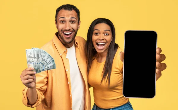 兴奋的年轻黑人男人和女人中了彩票 拿着一堆钞票 背景是黄色的 屏幕是黑色的智能手机 模仿着 拼凑着 — 图库照片