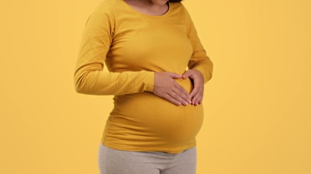 爱和怀孕 一个无法辨认的孕妇用手在她的大肚子上为心脏做手势 模仿心跳 背景黄色 动作缓慢的特写镜头 — 图库视频影像