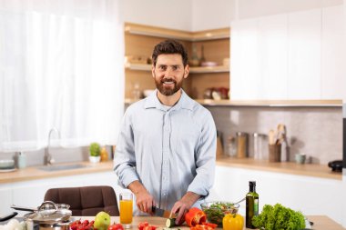 Gülümseyen, yetişkin, Avrupalı sakallı adam şef modern mutfak içinde salata için organik sebzeler kesiyor. Evde sağlıklı yemek pişirmek, sağlık, diyet ve gıda blogu