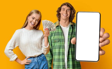 Neşeli hippiler sarıda başarıyı kutlayan genç adam ve kadın internette kumar oynayan çiftler, cep telefonlarını beyaz ekranlı gösteriyorlar ve bir sürü dolar, sarı arka plan, maket, stüdyo çekimi.