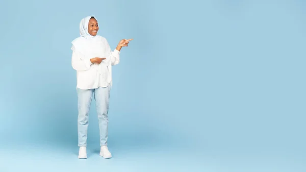 stock image Look there. Full length shot of african american muslim woman pointing fingers aside at free space for text or design, standing on blue studio background, panorama