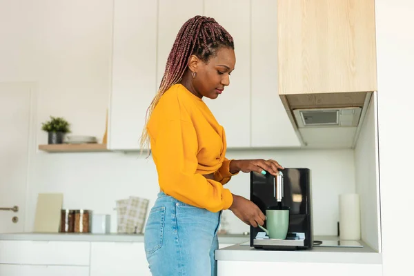stock image Young african american woman using modern coffee machine, making drink in the morning, standing in kitchen at home, free copy space, side view shot