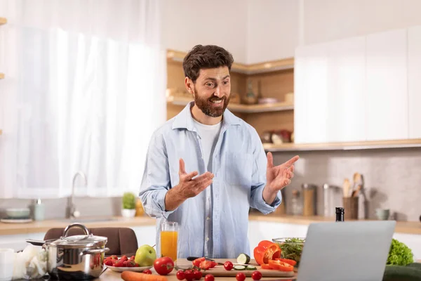 快乐的中年男子留着胡子 有视频通话 为食物博客制作视频 为双手做手势 在现代厨房内部准备健康的饭菜 家庭自制食品 保健和装置 — 图库照片