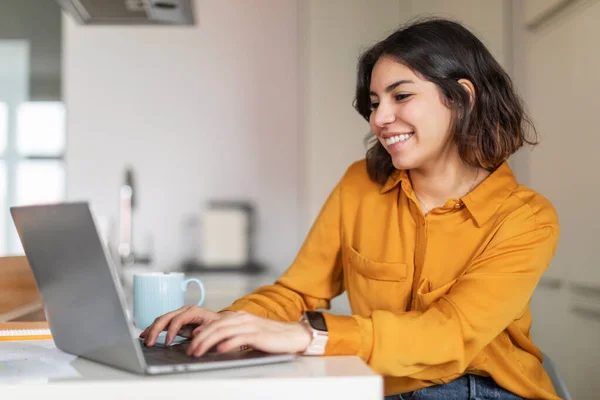Remote Work. Young Arab Female Freelancer Working With Laptop In Kitchen Interior At Home, Smiling Middle Eastern Woman Using Computer For Telecommuting, Enjoying Online Job, Copy Space