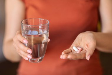 Tanınmayan bir kadın elinde bardak su ve haplar tutarken, güzelliği ve dokunulmazlığı için vitamin takviyesi alan ya da tıbbi tedavi alan bir kadının yakın plan fotoğrafı.