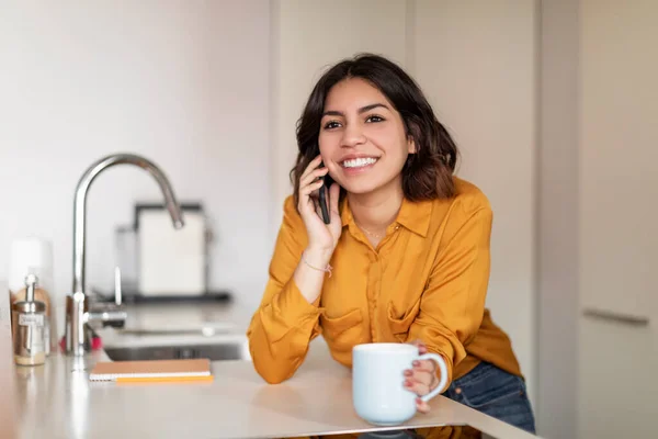 Gülümseyen Genç Arap Kadın Cep Telefonuyla Konuşuyor Mutfakta Kahve Içiyor — Stok fotoğraf