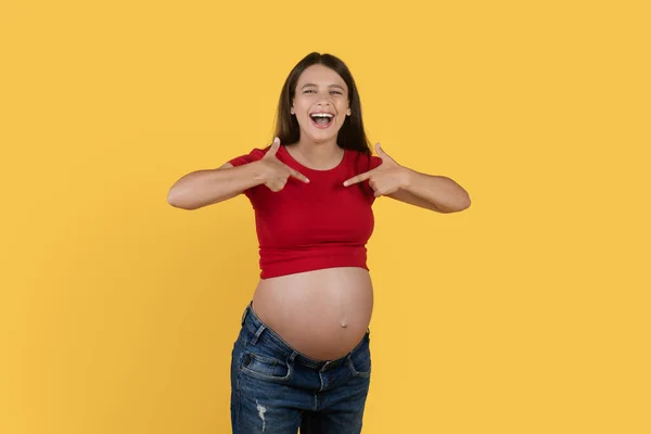 俺を選べ 明るく若い妊娠中の女性は彼女自身を指していると笑って 黄色の背景の上に孤立立ちながら 大きな腹を持つ積極的な期待の女性 スペースをコピー — ストック写真
