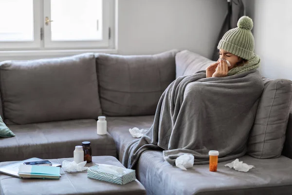暖かい毛布に覆われた病気の若い女性は 薬でテーブルの横に自宅でソファに座っています 病気の女性はナプキンに鼻水を吹いて 季節のインフルエンザと寒さに苦しんで スペースをコピー — ストック写真