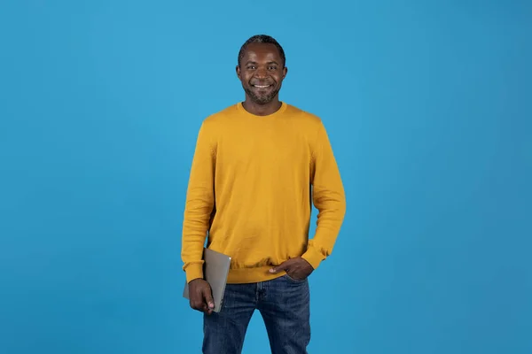 酷而快乐的英俊的非洲男子在休闲外向的美国成熟男子与现代笔记本电脑的蓝色工作室背景 微笑在相机 复制空间 技术和现代生活方式 — 图库照片