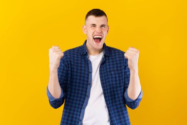 Duygusal, genç, beyaz bir adam sarı stüdyo arka planında bağırıp yumruklarını sallıyor. Zaferin kutlanması, sevinç duygusu konsepti