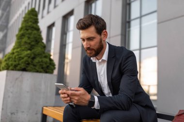 Ciddi, düşünceli, takım elbiseli, akıllı telefonda konuşan, mesaj okuyan, şehir caddesindeki bankta oturan Avrupalı genç bir menajer. Çalışma, finans ve modern iş uygulaması, sağlık hizmetleri