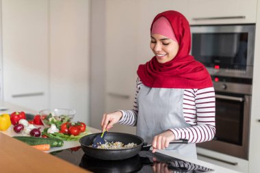 Müslüman eş, tesettürlü genç ve güzel bir kadın evde yemek yapmayı, taze sebzeleri doğramayı ve tavada bir şeyler kızartmayı seviyor.