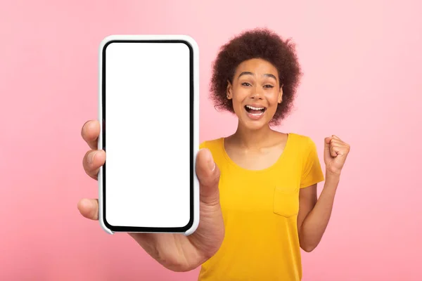 令人高兴的是 年轻的非洲卷曲女士带着空白屏幕展示了智能手机 做出了胜利 成功的姿态 在粉色背景下被孤立在工作室里 应用和装置 在线广告和提供 — 图库照片
