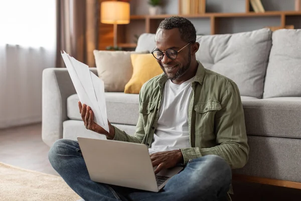 中高年アフリカ系アメリカ人男性がガラスにノートパソコンで読書をしている 紙仕事とビジネス 新しい通常 デバイスと契約 自宅オフィスでの契約の詳細 — ストック写真
