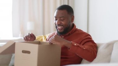 Kutuları açma konsepti. Heyecanlı Afrikalı Amerikalı adam teslimat kutusunu açıyor ve satın alınıyor, evde online alışveriş servisinin tadını çıkarıyor, çekim takip ediyor, yavaş çekim, serbest alan