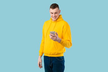 Mutlu genç adam cep telefonunda havalı cep telefonu uygulaması kullanıyor ya da akıllı telefonla mesajlaşıyor, mavi stüdyo arka planında internetten iletişim kuruyor. İletişim ve teknoloji