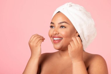 Afro-Amerikan kadın portresi, diş ipliği kullanan, gülümseyen, pembe stüdyo arka planında diş temizleyen, serbest alan. Diş sağlığı konsepti